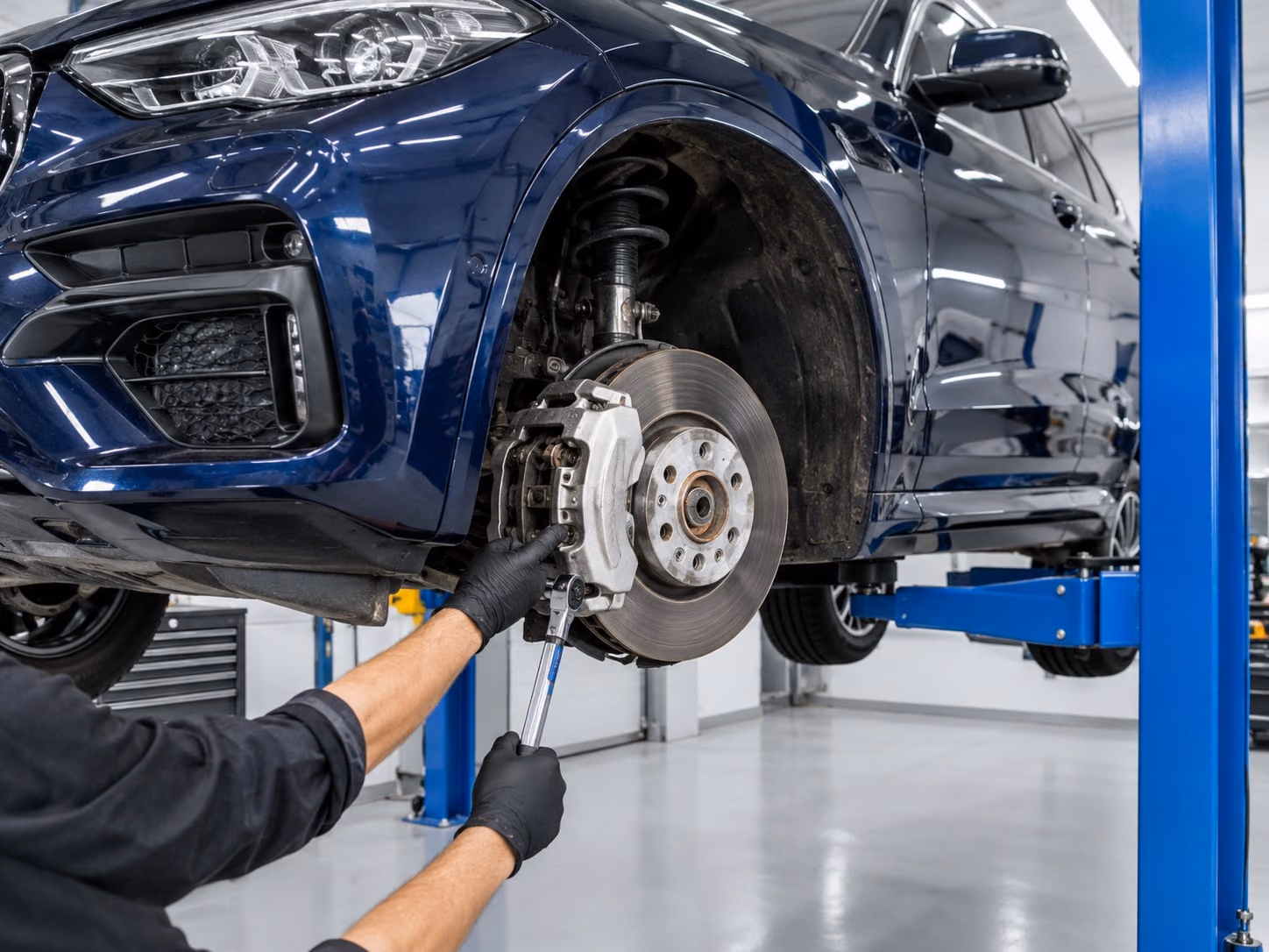 Mechanic's gloved hands tightening the brake calliper of a dark blue SUV raised on a lift